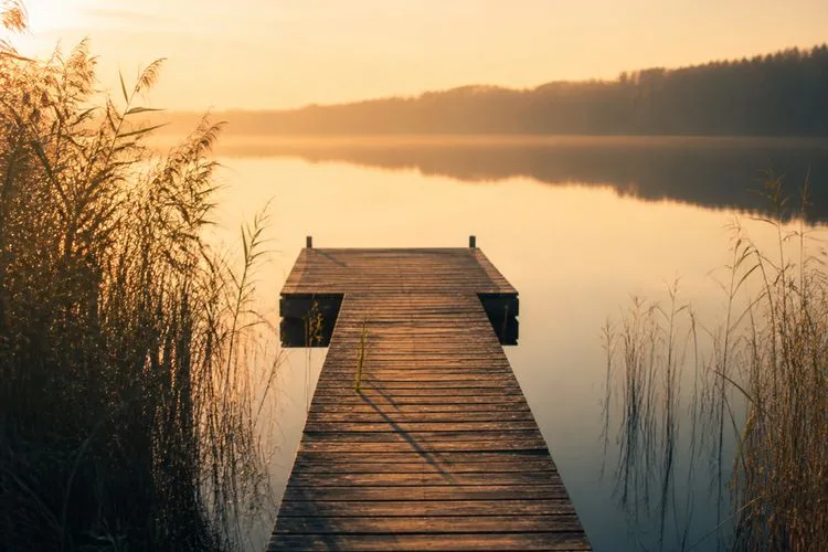 An empty wooden swim dock over a still lake in late-August evening light