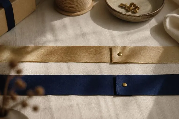 Two parallel ribbons on linen, gold and blue, with their seams offset from each other and marked by small brass pins