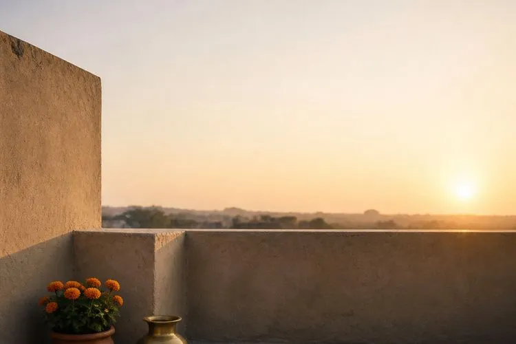 An empty rooftop terrace at sunrise, with marigolds in a clay pot and a brass vessel on bare stone.